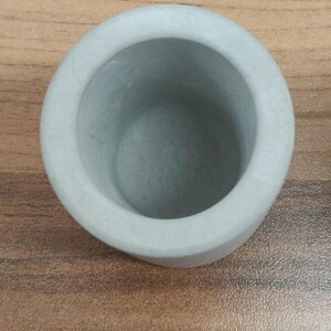 May include: A small, light gray concrete planter pot. The pot is round and has a smooth, slightly textured surface.