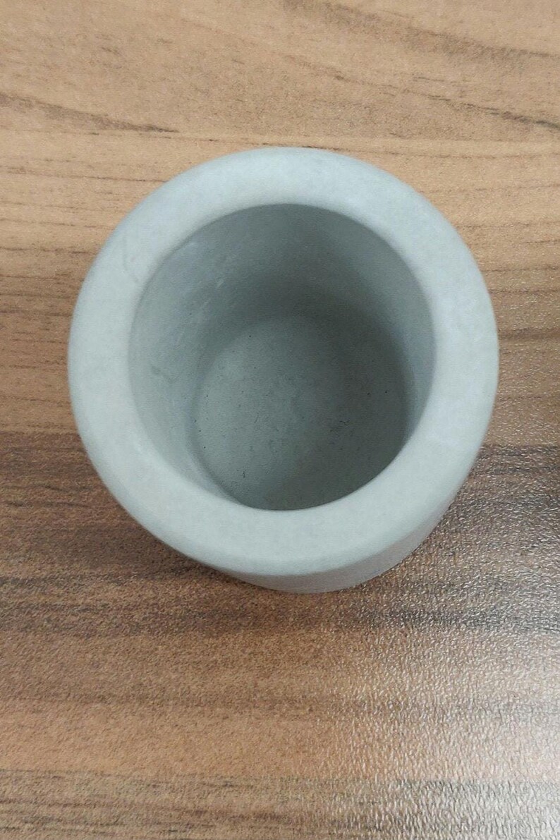 May include: A small, light gray concrete planter pot. The pot is round and has a smooth, slightly textured surface.
