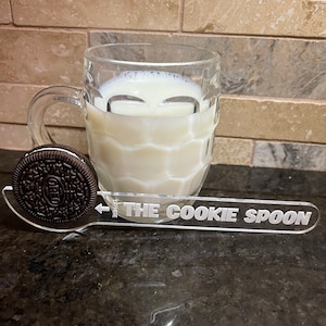 May include: A clear glass mug filled with milk, a black and white Oreo cookie, and a clear acrylic cookie dipping spoon with the text "THE COOKIE SPOON" printed on it.