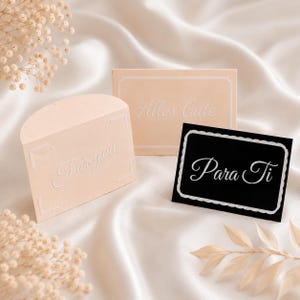 May include: Two light peach-colored cards and one black rectangular card. One peach card has a rounded top and the text For you. The other peach card has the text Alles Gute. The black card features a scalloped white border and the text Para Ti.