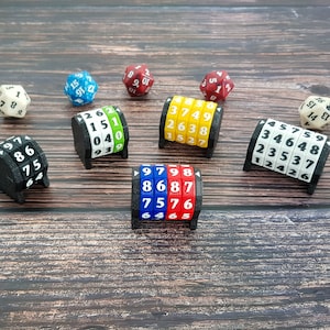 Könnte beinhalten: Ein Satz von sechs schwarzen und weißen Zahlendrehern mit Zahlen in verschiedenen Farben. Die Dreher befinden sich auf einer Holzoberfläche. Die Zahlen auf den Drehern sind 1, 2, 3, 4, 5, 6, 7, 8, 9, 0.