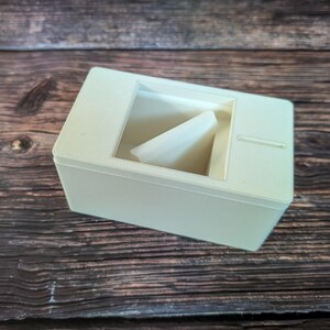 May include: A white plastic box with a small opening on the top. The box has a white plastic insert inside.