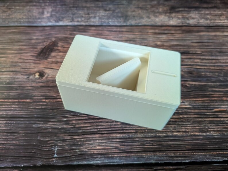 May include: A white plastic box with a small opening on the top. The box has a white plastic insert inside.