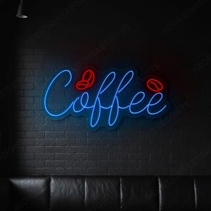 May include: A neon sign that says "Coffee" in blue script with red coffee bean accents. The sign is mounted on a black brick wall in a coffee shop or cafe. The shop has black leather seating and a dark wood table.