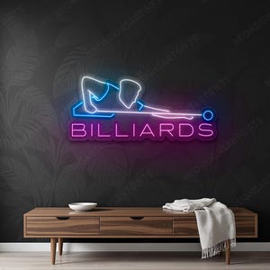 Może przedstawiać: Neonowy znak z napisem "BILLIARDS" w kolorze różowym i fioletowym. Znak przedstawia niebiesko-biały kontur osoby grającej w bilard. Znak jest zamontowany na ciemnej ścianie nad drewnianą szafką.