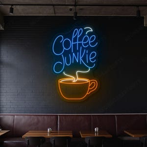 May include: A neon sign with the words "Coffee Junkie" in blue script above an orange coffee cup with steam. The sign is mounted on a black brick wall in a cafe setting.
