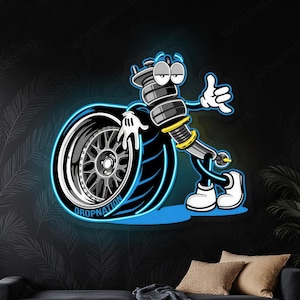 Pode incluir: Uma placa de néon com um personagem de desenho animado feito de peças de carro, incluindo um pneu e um amortecedor. O personagem é contornado em néon azul, com o texto "DROP NATION" no pneu. O fundo é preto.