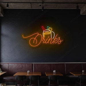 Może przedstawiać: Neonowy szyld z napisem "Drinks" w kursywie, któremu towarzyszy podświetlony obraz napoju w słoiku ze słomką. Znak jest pomarańczowy i żółty, zamontowany na czarnej ceglanej ścianie w restauracji.