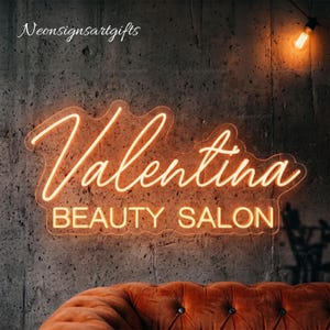 May include: A warm orange neon sign mounted on a dark gray concrete wall. The sign displays the text Valentina in a cursive script font, with the words BEAUTY SALON in a block sans-serif font underneath. The text Neonsignsartgifts is visible.