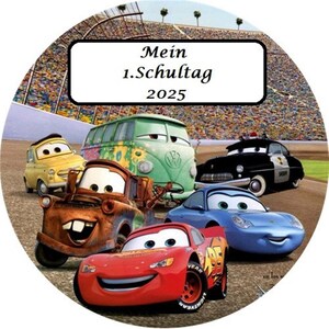 Peut inclure: Image circulaire avec des personnages de Cars. On y voit Flash McQueen, Martin et d'autres voitures animées. Un rectangle blanc en haut affiche le texte "Mein 1.Schultag 2025". L'arrière-plan montre un circuit.