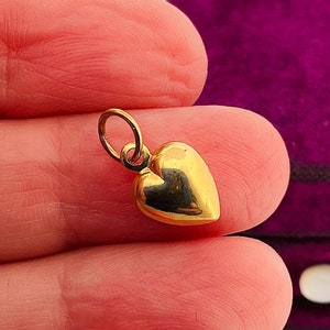 May include: A small gold heart charm pendant. The charm is in the shape of a heart and has a loop at the top for attaching to a chain or bracelet.
