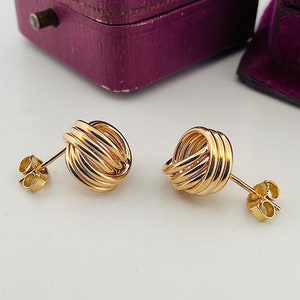 May include: A pair of gold knot-shaped earrings. The earrings are made of thick, twisted wire.