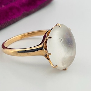 Pu&ograve; includere: Un anello d'oro con una grande gemma ovale e traslucida. La fascia dell'anello &egrave; in oro lucido e la gemma &egrave; tenuta da delicate griffe. La gemma ha un aspetto morbido e perlaceo.