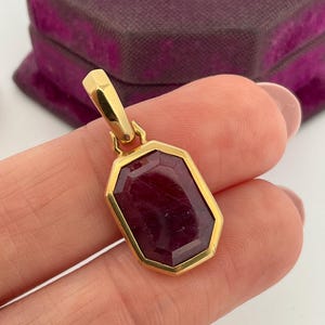 May include: A gold pendant featuring an octagonal-cut deep red gemstone set in a polished gold frame with a matching gold bail at the top, designed for attachment to a necklace chain.