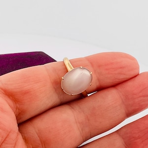Pu&ograve; includere: Un anello d'oro con una grande gemma ovale rosa pallido. La gemma &egrave; incastonata in una semplice montatura a quattro griffe. L'anello &egrave; presentato su uno sfondo bianco.