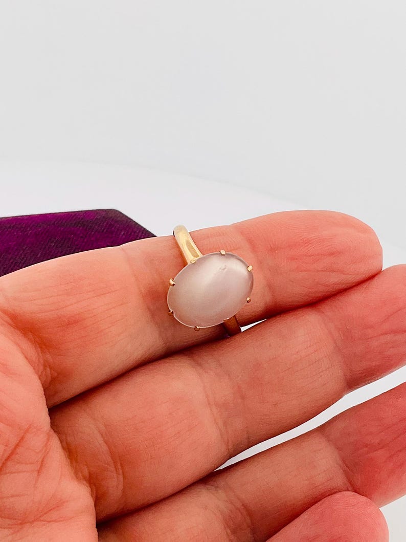 Pu&ograve; includere: Un anello d'oro con una grande gemma ovale rosa pallido. La gemma &egrave; incastonata in una semplice montatura a quattro griffe. L'anello &egrave; presentato su uno sfondo bianco.