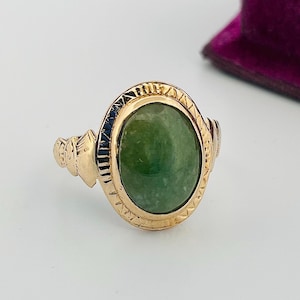 May include: A gold ring featuring an oval green gemstone set in an intricate gold design.