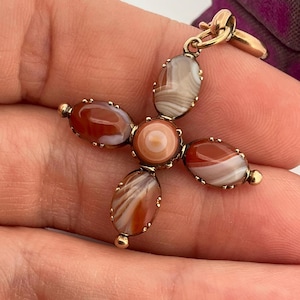 May include: A gold pendant featuring a central circular agate stone surrounded by four oval-shaped agate stones arranged in a cross pattern. Each stone displays banded patterns in shades of reddish-brown, white, and tan, all set in a gold metal frame.