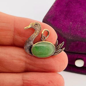 May include: A gold pendant featuring a jade green oval stone set in a swan design.