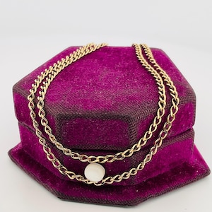 May include: A gold chain necklace with a single white pearl pendant. The necklace is displayed in a purple velvet box.