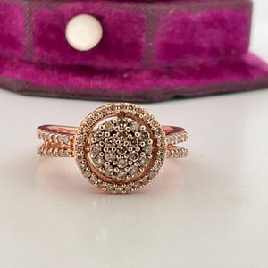 May include: A rose gold ring with a round centre stone surrounded by smaller diamonds. The ring has a double band.