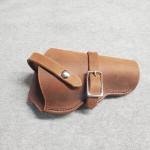 May include: A brown leather holster with a silver buckle and a snap closure.