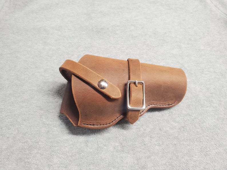 May include: A brown leather holster with a silver buckle and a snap closure.