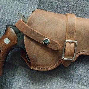 May include: A brown leather holster with a silver buckle and a black revolver inside.