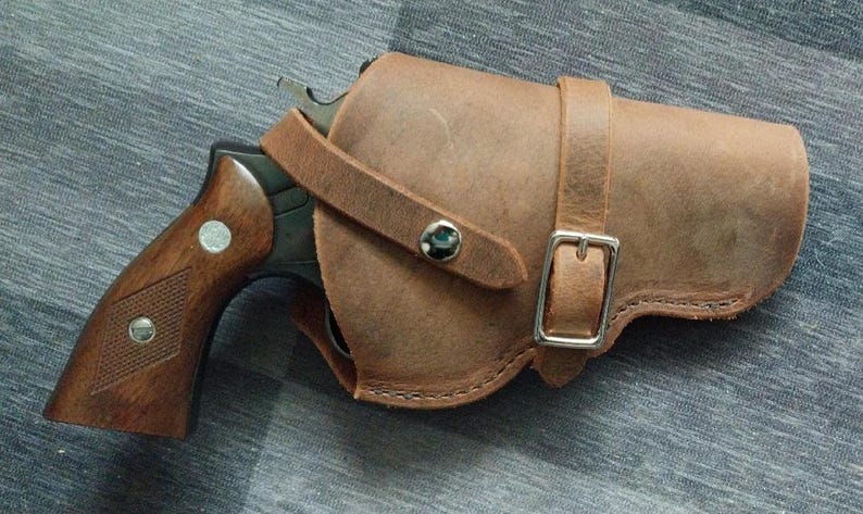 May include: A brown leather holster with a silver buckle and a black revolver inside.