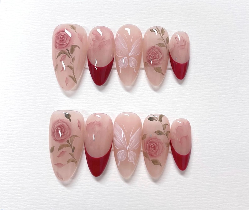 May include: Set of ten false nails with a red tip and a floral design. The design features pink roses, leaves, and a butterfly.