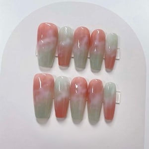 May include: Set of ten pink and white swirl press-on nails. The nails are long and have a cloudy, marbled design.