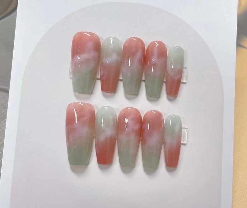 May include: Set of ten pink and white swirl press-on nails. The nails are long and have a cloudy, marbled design.