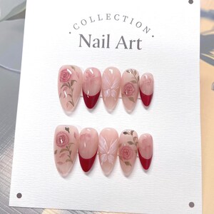 May include: A set of ten fake nails with a floral design. The nails are a light pink color with a red tip. The floral design features pink roses and butterflies.