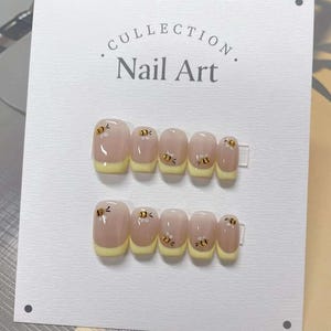 May include: A set of ten press-on nails with a light pink base and a yellow tip. Each nail features a small bee design with black and yellow accents.