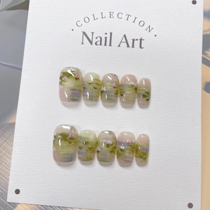 May include: A set of ten fake nails with a light green and pink water lily design. The nails are displayed on a white card with the text "COLLECTION Nail Art".