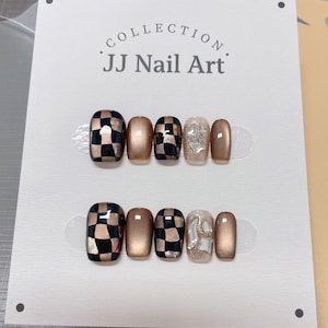 May include: Two sets of false nails on a white card. The nails feature a mix of designs, including a black and gold checkerboard pattern, solid gold, and a silver textured design. The card reads "COLLECTION JJ Nail Art."
