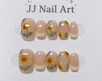 May include: A set of ten press-on nails from the JJ Nail Art collection, featuring a nude base with hand-painted yellow sunflower designs and cream-colored French tips on select nails, arranged in two rows on a white display card.