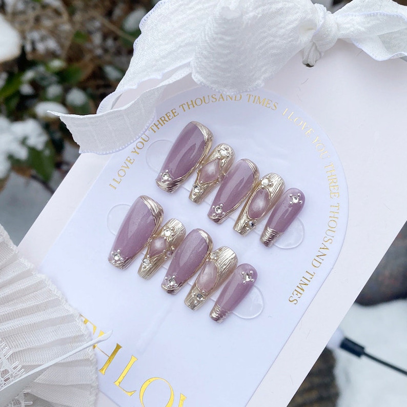 Peut inclure: Ensemble de dix faux ongles avec une base violet clair, des accents argent&eacute;s et des embellissements nacr&eacute;s. Les ongles sont pr&eacute;sent&eacute;s sur une carte blanche avec le texte "I love you three thousand times I love you three thousand times".