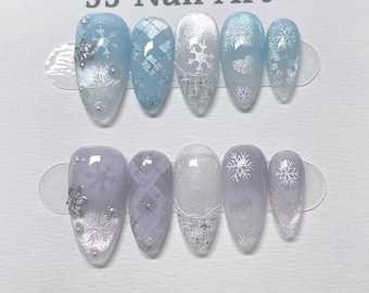 May include: A set of ten artificial nails with a winter theme. The nails feature a variety of designs, including snowflakes, glitter, and geometric patterns. The color palette includes shades of blue, white, and silver. The text "JJ Nail Art" is at the top.