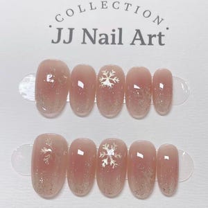 May include: Artificial nail set with a light pink gradient and silver glitter. Each nail features a snowflake design. The text "COLLECTION" and "JJ Nail Art" is at the top.