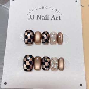 May include: Two sets of false nails on a white card. The nails feature a mix of designs, including a black and gold checkerboard pattern, solid gold, and a silver textured design. The card reads "COLLECTION JJ Nail Art."