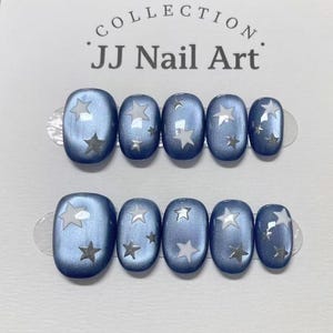 May include: A set of ten press-on nails from the JJ Nail Art collection, featuring a metallic blue finish with white and silver star patterns. The nails are arranged in two rows of five, displaying various sizes with a smooth, glossy surface.
