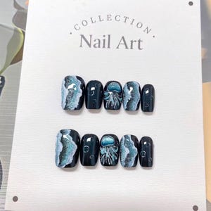 May include: A set of press-on nails with a dark teal base. Some nails feature a swirling blue and white design, while others showcase a jellyfish illustration. The text "Collection Nail Art" is visible on the display card.