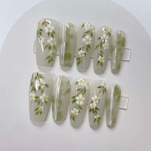 May include: Set of ten white press-on nails with a green and white floral design.