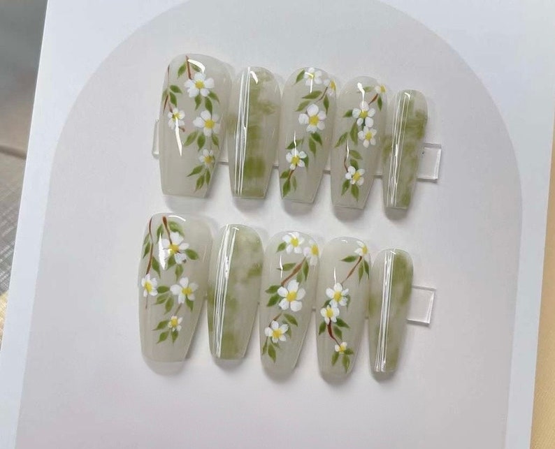 May include: Set of ten white press-on nails with a green and white floral design.