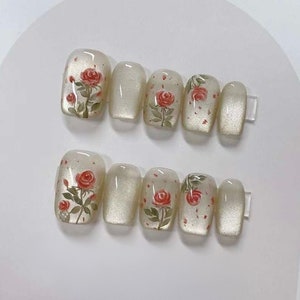 May include: Set of ten false nails with a white base and a floral design featuring red roses and green leaves.