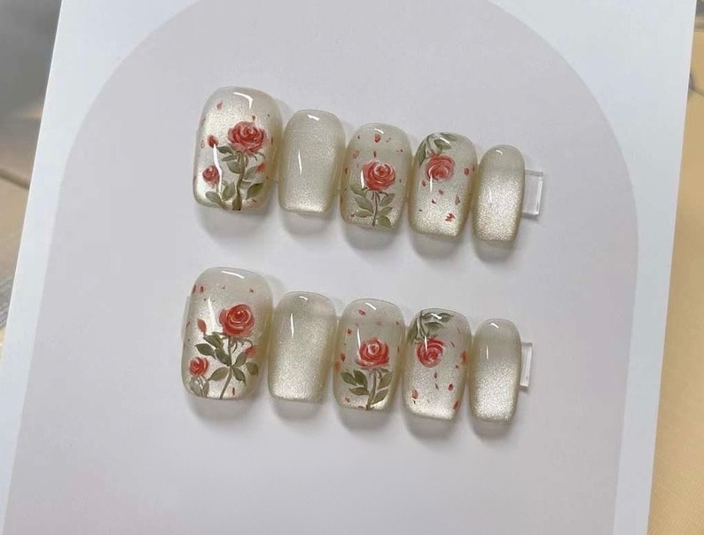 May include: Set of ten false nails with a white base and a floral design featuring red roses and green leaves.