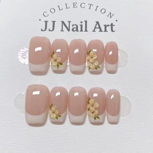 May include: A set of ten press-on nails with a French manicure design featuring a nude base and white tips. Some nails are decorated with small, raised yellow flower accents with green leaves. The text JJ Nail Art Collection is printed above.