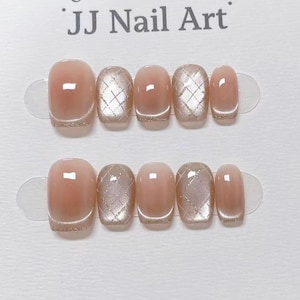 May include: Two sets of artificial nails. Each set has five nails in a light pink hue, with a glittery gold border. Some nails feature a silver diamond pattern. The text "JJ Nail Art" is at the top.