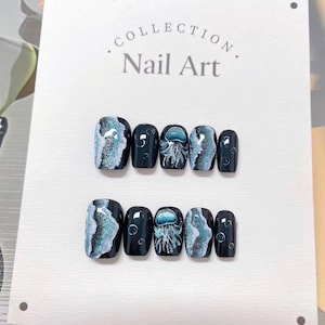 Peut inclure: Ensemble de faux ongles avec une base bleu fonc&eacute;. Certains ongles pr&eacute;sentent un motif tourbillonnant bleu et blanc, tandis que d'autres pr&eacute;sentent une illustration de m&eacute;duse. Le texte "Collection Nail Art" est visible.